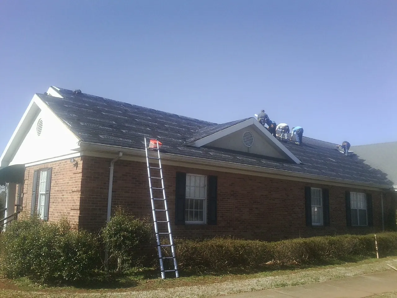 Crew tearing shingles off a brick ranch roof with a ladder set — Emergency Roof Repair work by our crew in Wisconsin Rapids