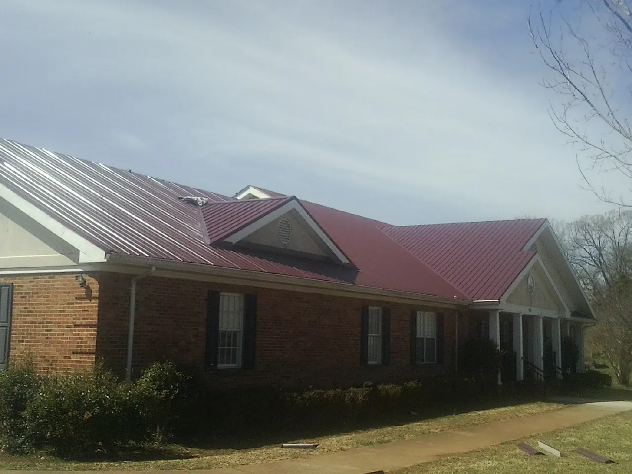 Red metal roof with gabled entries on a long brick building, from a Hail Damage Roof Repair job in Wisconsin Rapids