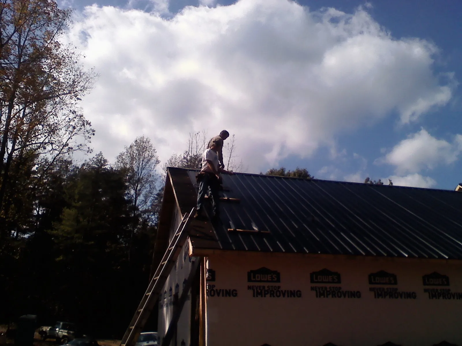 Roofer fastening dark metal panels high against a cloudy sky, from a Roof Inspection job in Wisconsin Rapids