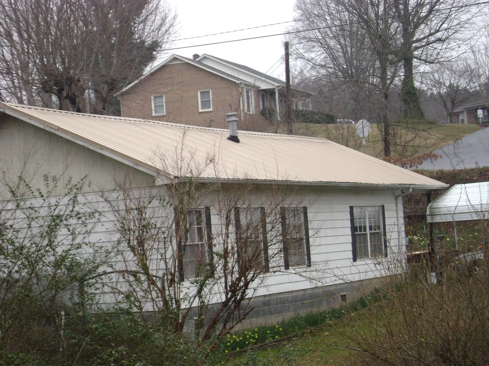 Tan metal roof on a white sided house set into a hillside — Commercial Roofing by Roofing Brothers in Wisconsin Rapids